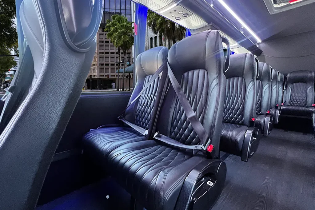 Close-up of leather bus seats under blue ambient lighting, with palm trees visible outside.