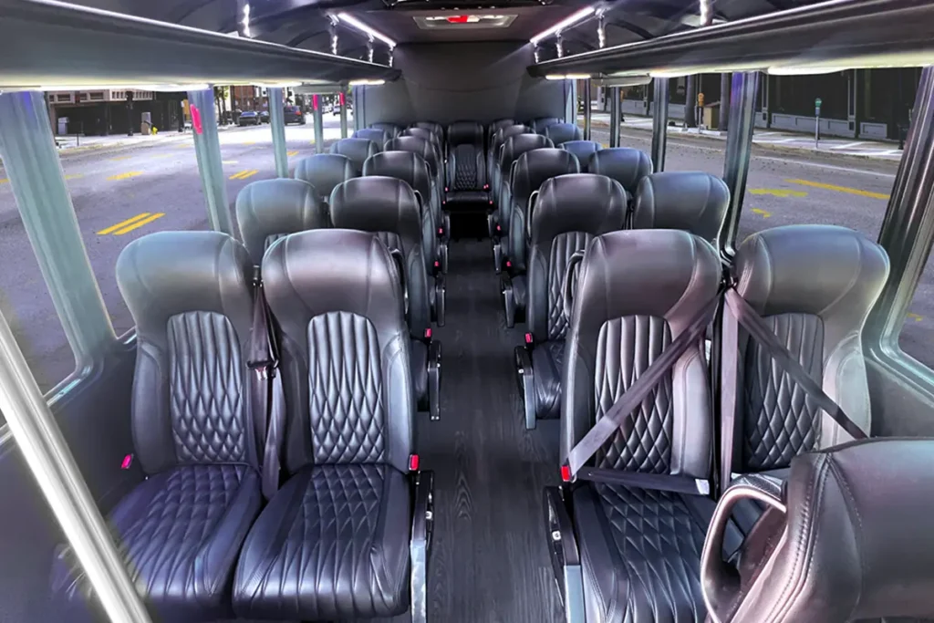 Minibus interior with diamond-stitched black leather seats and a city street visible outside.