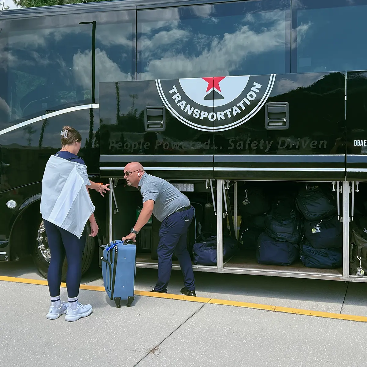 Attendant loading passenger luggage into a motorcoach's storage compartment.