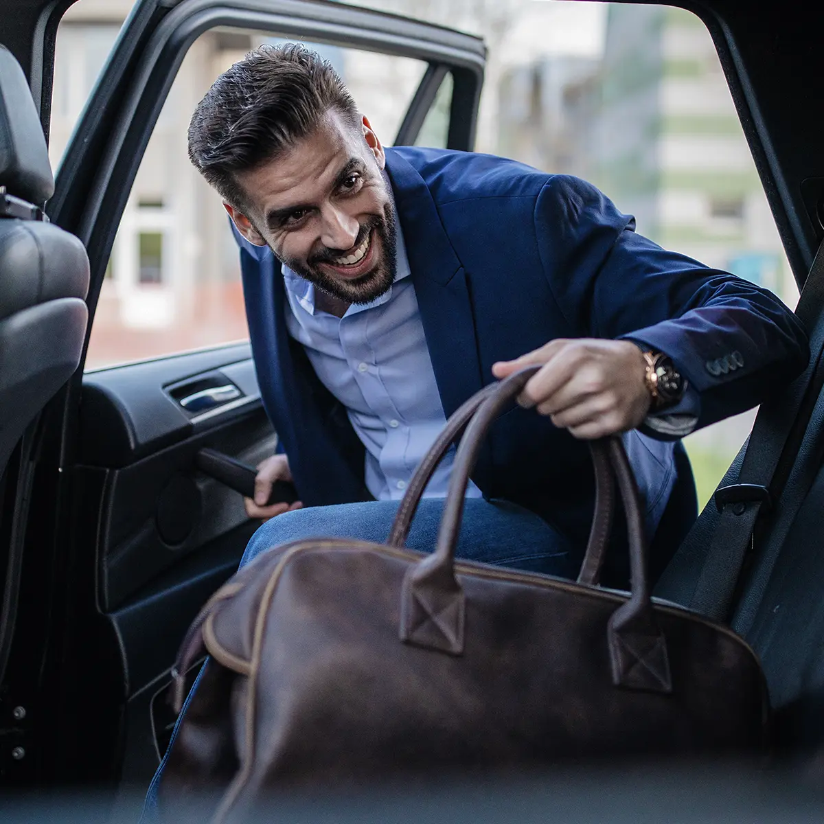 Smiling businessman entering a car with a leather duffel bag.