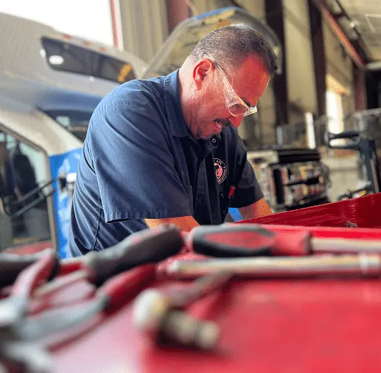Mechanic in safety glasses servicing a vehicle in a garage.