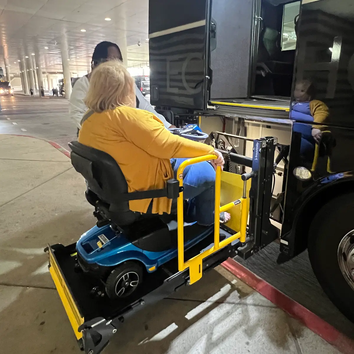 Woman on a mobility scooter being lifted onto a bus.