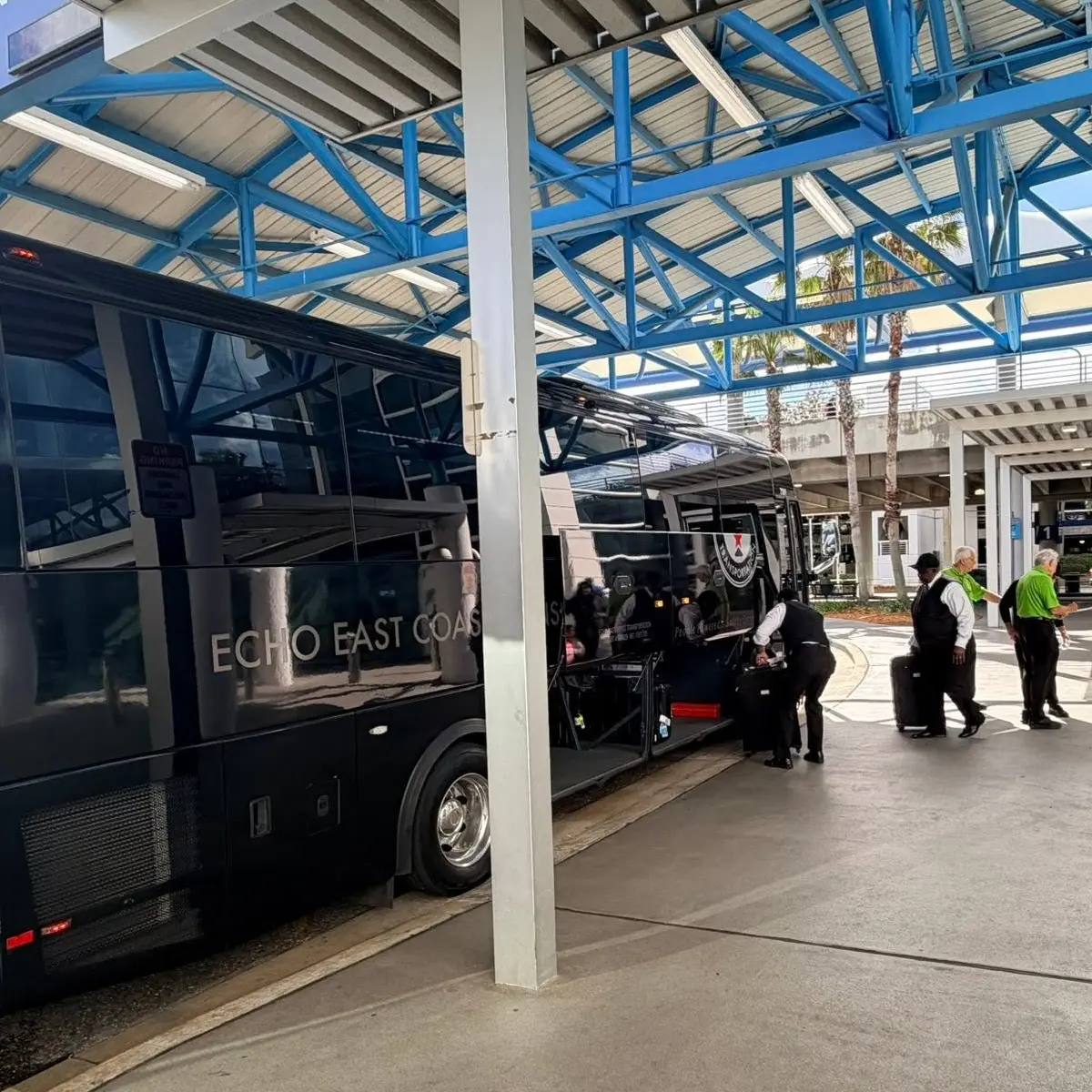 Chauffeurs loading luggage into an Echo East Coast Transportation motorcoach at an airport curb.